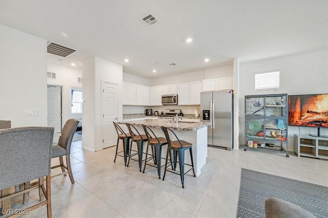 kitchen with a kitchen island with sink, stainless steel appliances, light stone counters, and visible vents