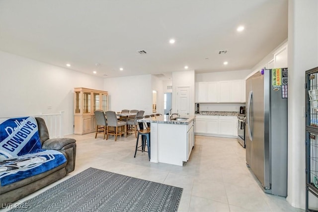 kitchen with a sink, visible vents, white cabinets, appliances with stainless steel finishes, and light stone countertops