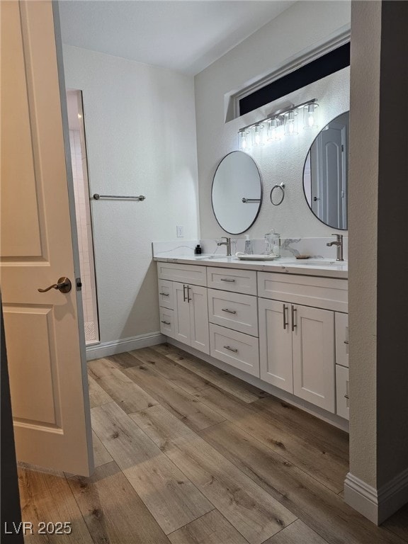 full bath featuring a sink, double vanity, baseboards, and wood finished floors