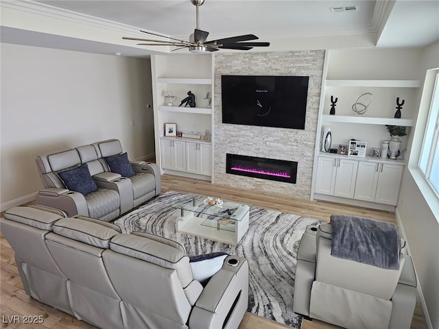 living room featuring built in features, crown molding, visible vents, light wood-style floors, and a stone fireplace