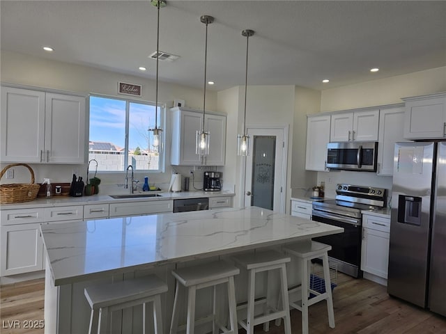 kitchen with stainless steel appliances, light wood-type flooring, white cabinetry, and a sink