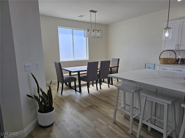 dining area with a notable chandelier, light wood finished floors, visible vents, and baseboards