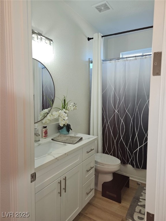 bathroom featuring toilet, wood finished floors, vanity, visible vents, and shower / bathtub combination with curtain