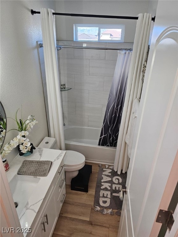 bathroom with a textured wall, toilet, wood finished floors, vanity, and shower / bathtub combination with curtain