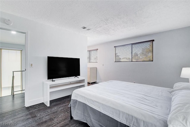 bedroom featuring dark wood-style floors, a textured ceiling, visible vents, and baseboards