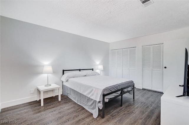 bedroom with dark wood-style floors, a textured ceiling, visible vents, and two closets