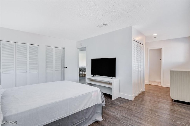 bedroom with baseboards, visible vents, wood finished floors, a textured ceiling, and multiple closets