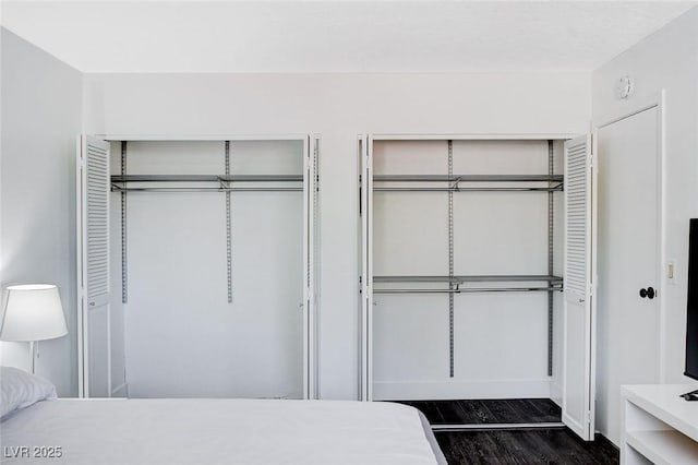 bedroom with baseboards, dark wood-style flooring, and two closets