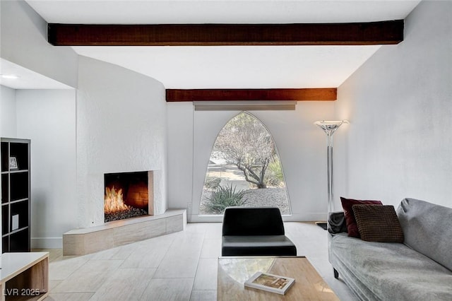 living area featuring a lit fireplace, beam ceiling, and baseboards