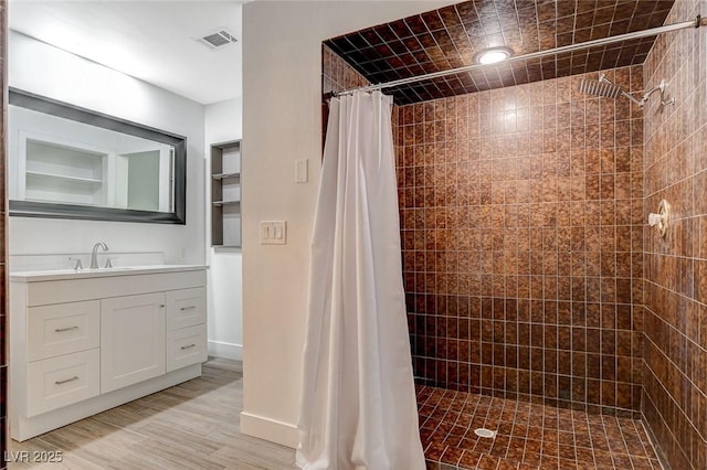 full bathroom with wood finished floors, visible vents, vanity, and tiled shower