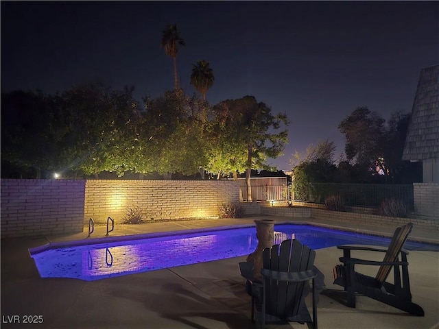 pool at night featuring a patio area, a fenced backyard, and a fenced in pool