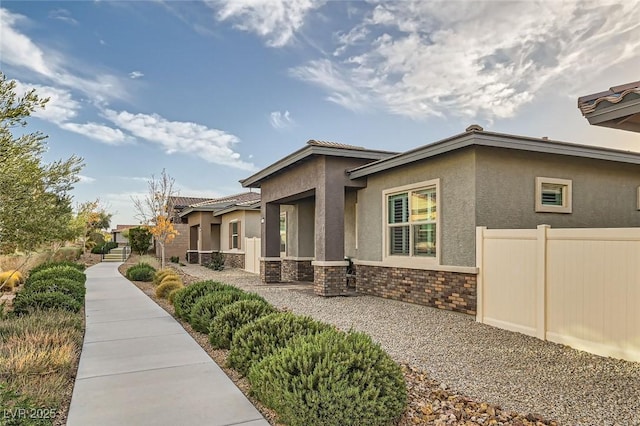 view of side of property featuring stone siding, fence, and stucco siding