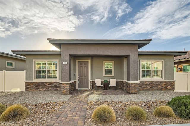 view of front facade with brick siding, fence, and stucco siding