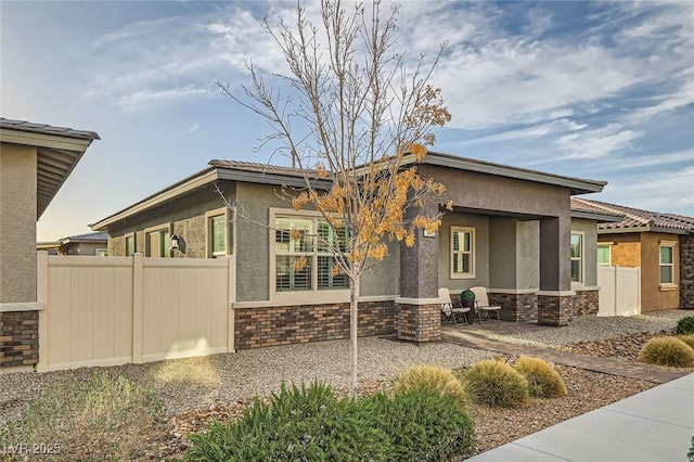 view of side of home with stone siding, a patio area, fence, and stucco siding