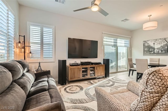 living room with light wood-style floors, ceiling fan, visible vents, and baseboards