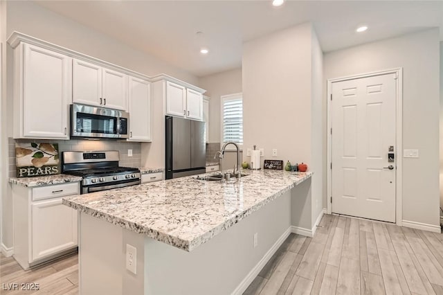 kitchen with decorative backsplash, appliances with stainless steel finishes, a peninsula, white cabinetry, and a sink