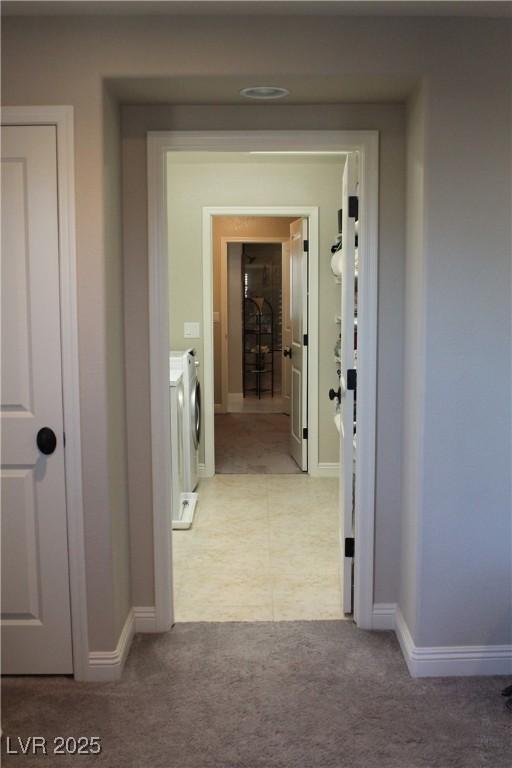 hallway with washing machine and dryer, light colored carpet, and baseboards