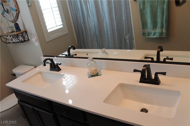 bathroom with toilet, double vanity, and a sink