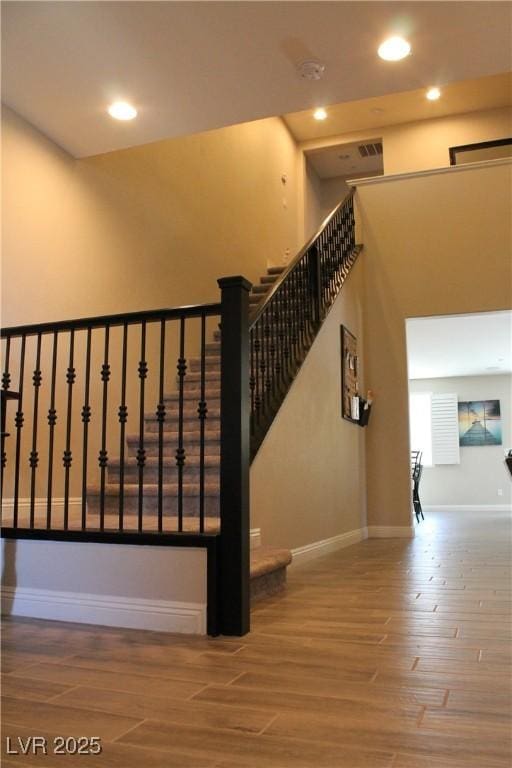 stairway featuring recessed lighting, a high ceiling, baseboards, and wood finished floors