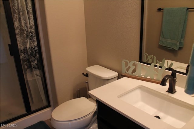 full bath featuring a textured wall, vanity, a shower stall, and toilet