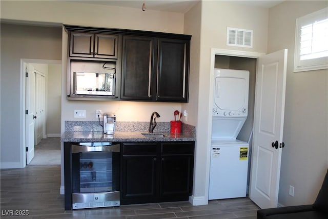 kitchen with wine cooler, stacked washer / drying machine, visible vents, stone countertops, and a sink