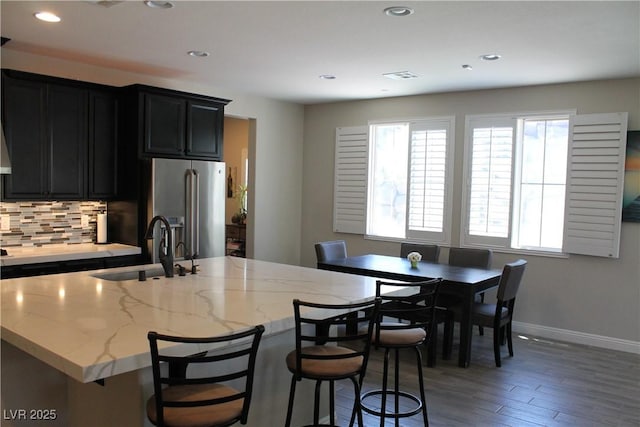 kitchen featuring dark cabinets, a sink, light wood-style floors, high end fridge, and decorative backsplash