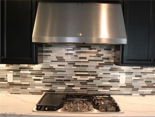 interior details with light stone counters, extractor fan, dark cabinetry, stainless steel gas cooktop, and backsplash