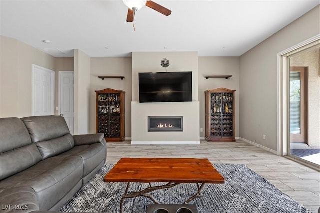 living area featuring wood finish floors, a glass covered fireplace, a ceiling fan, and baseboards