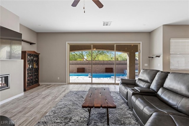 unfurnished living room featuring baseboards, visible vents, a ceiling fan, a glass covered fireplace, and wood finished floors