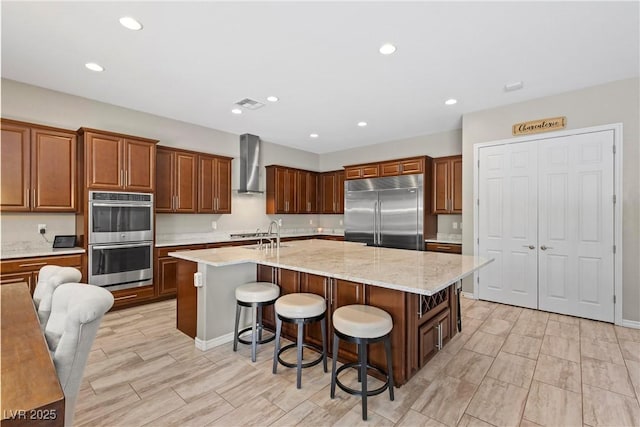 kitchen with a spacious island, visible vents, a kitchen breakfast bar, appliances with stainless steel finishes, and wall chimney range hood