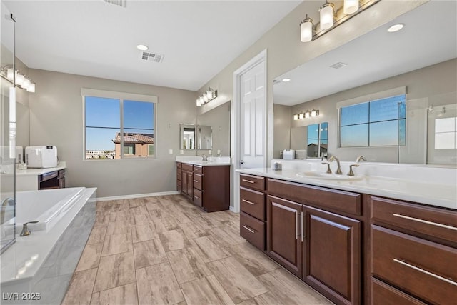 bathroom with a garden tub, visible vents, two vanities, and a sink