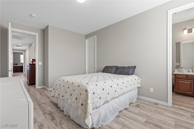 bedroom with connected bathroom, light wood-style flooring, and baseboards