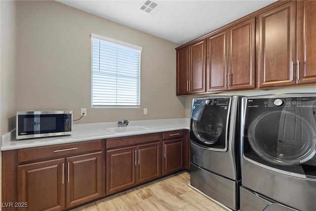 washroom with separate washer and dryer, a sink, visible vents, light wood-style floors, and cabinet space