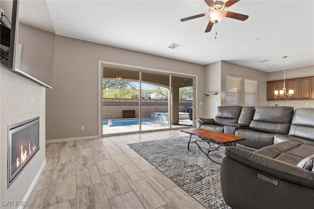 living room with baseboards, visible vents, a glass covered fireplace, wood tiled floor, and ceiling fan with notable chandelier