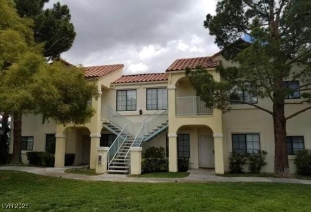 view of front facade with a tile roof, a front yard, stairway, and stucco siding