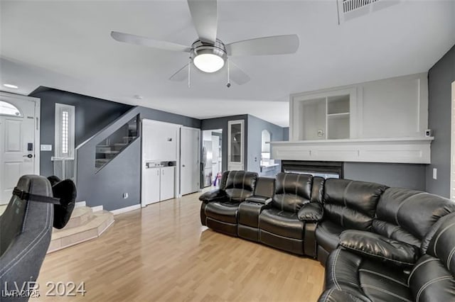 living area featuring a fireplace, visible vents, stairway, a ceiling fan, and light wood-type flooring