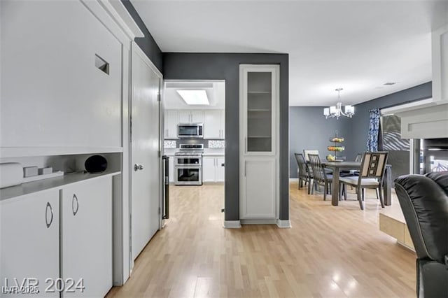 kitchen with light wood-style flooring, a notable chandelier, white cabinets, appliances with stainless steel finishes, and decorative light fixtures