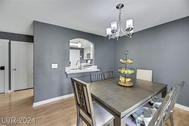 dining area with arched walkways, light wood finished floors, a notable chandelier, and baseboards