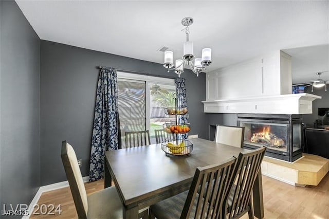 dining room with light wood-style floors, a glass covered fireplace, a notable chandelier, and baseboards