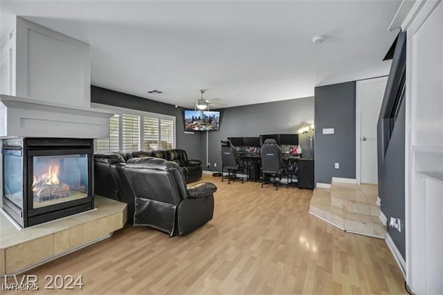 living room featuring light wood-type flooring, baseboards, ceiling fan, and a multi sided fireplace