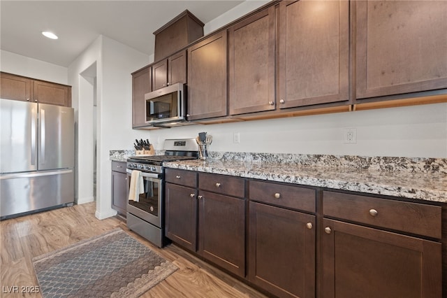 kitchen with stainless steel appliances, dark brown cabinetry, light stone counters, and light wood finished floors