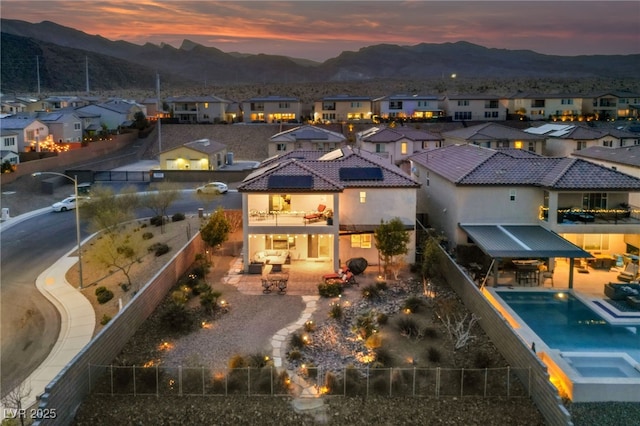 back of house at dusk featuring a fenced backyard, a residential view, a mountain view, and a patio