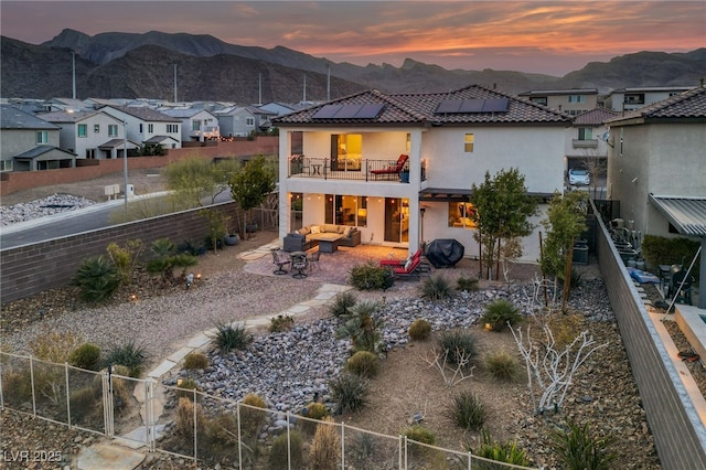 back of house at dusk with roof mounted solar panels, a fenced backyard, a patio, and an outdoor hangout area