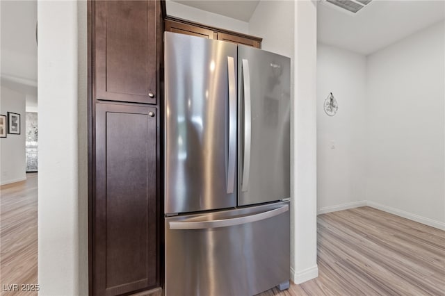 kitchen featuring visible vents, baseboards, freestanding refrigerator, dark brown cabinets, and light wood-type flooring