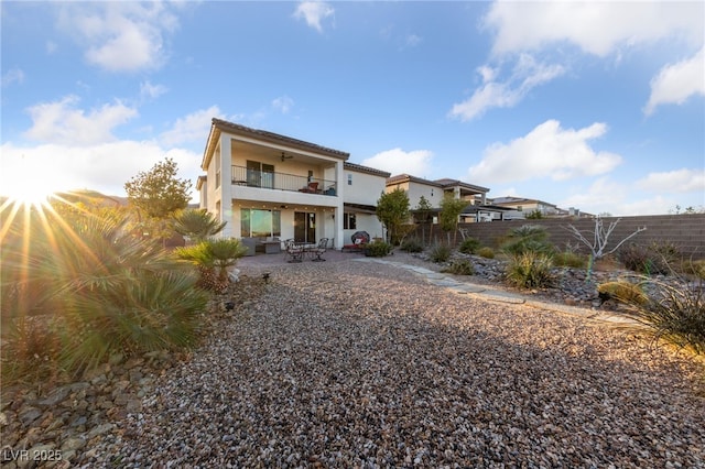 back of property with stucco siding, a patio area, fence, a balcony, and ceiling fan