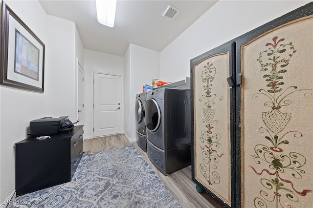 laundry room with light wood-type flooring, laundry area, washing machine and dryer, and visible vents