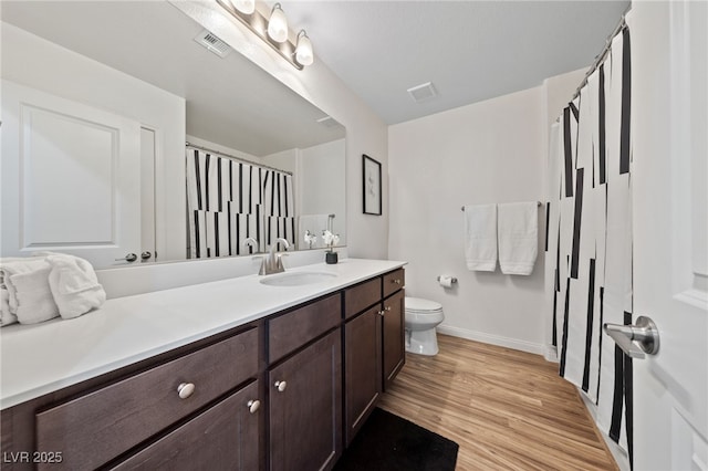 bathroom featuring toilet, vanity, wood finished floors, and visible vents