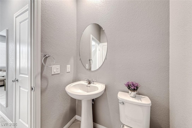 bathroom featuring a textured wall, toilet, and baseboards