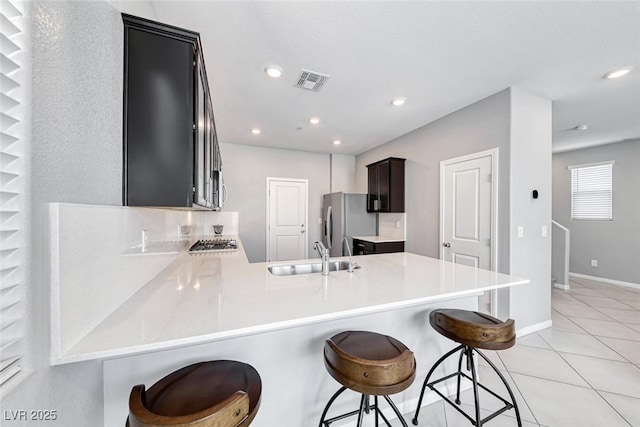 kitchen featuring stainless steel appliances, visible vents, a sink, a peninsula, and a kitchen breakfast bar