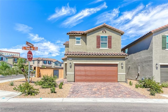 mediterranean / spanish home with a garage, a tile roof, decorative driveway, and stucco siding